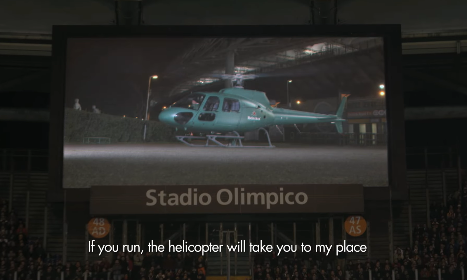 Groene helikopter op groot scherm in stadion met tekst onderaan.