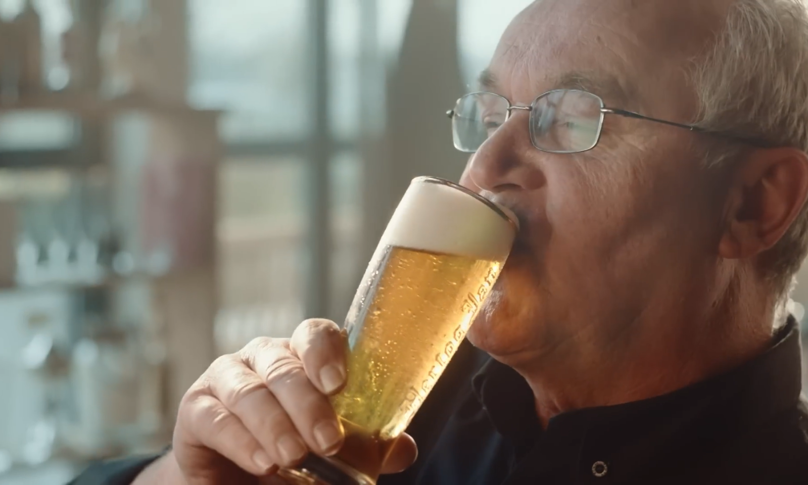 Man drinkt een glas Hertog Jan pilsener met schuimkraag.