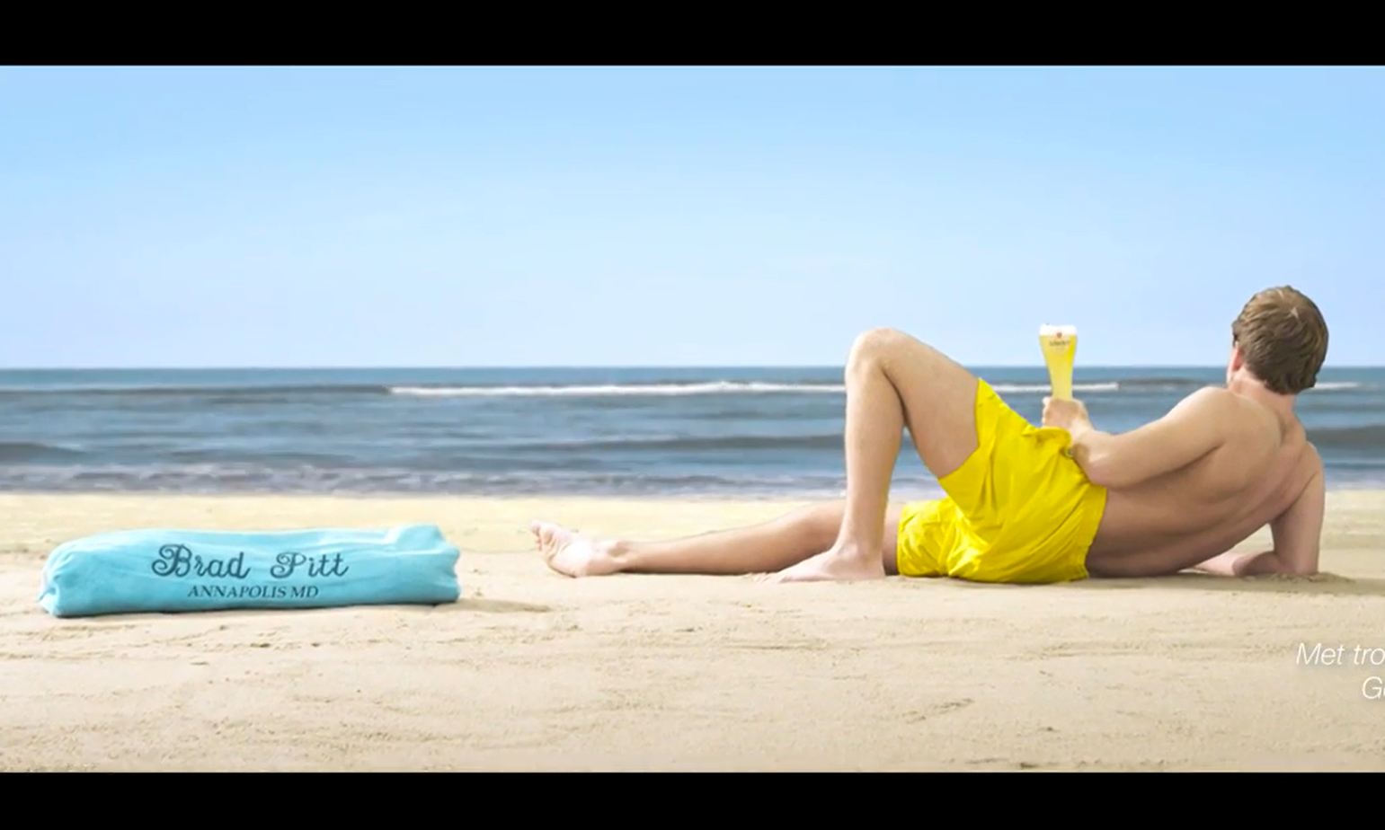 Persoon in gele zwembroek liggend op het strand met een glas bier.