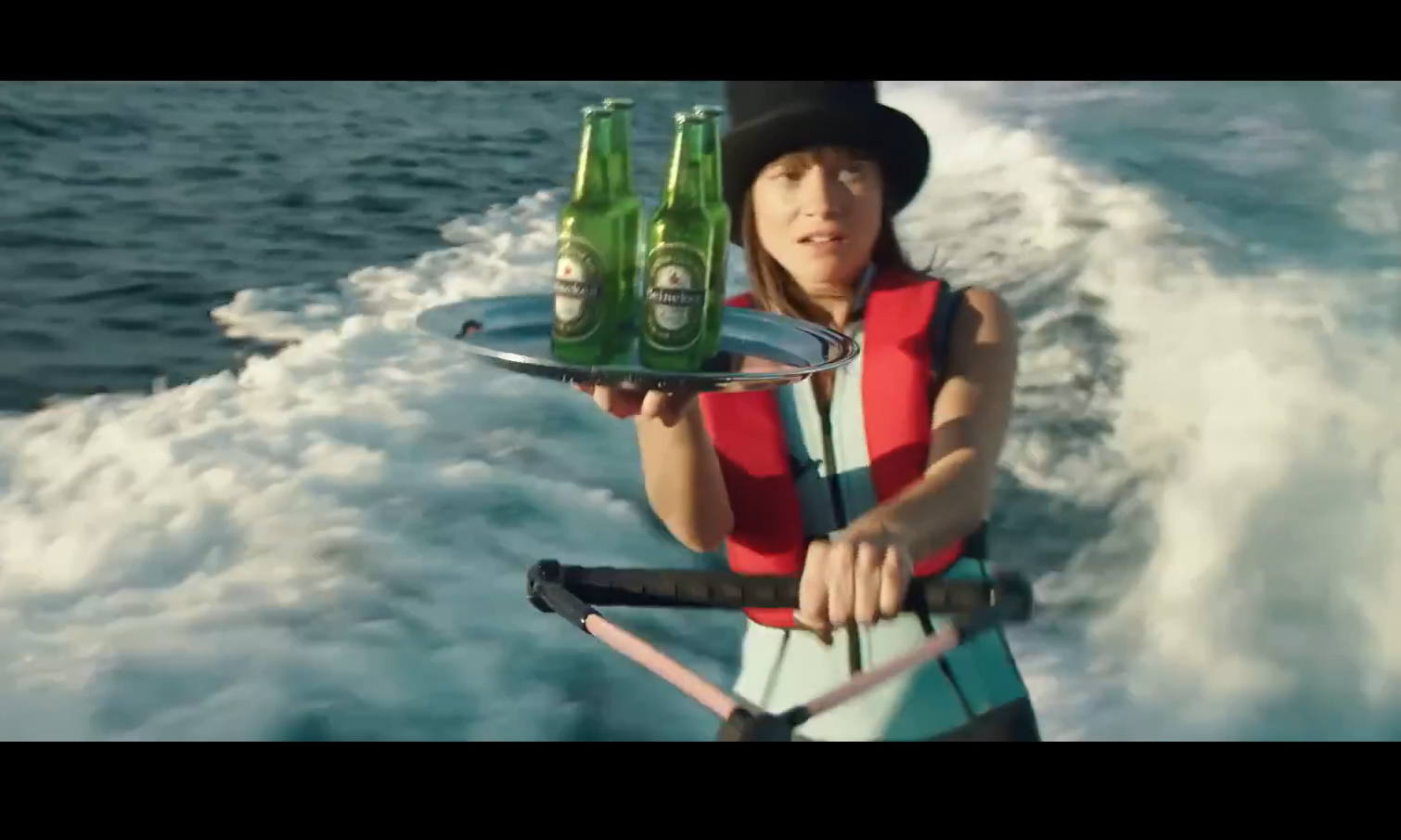 Persoon op waterski biedt twee Heineken-bierflesjes aan op een zilveren dienblad.