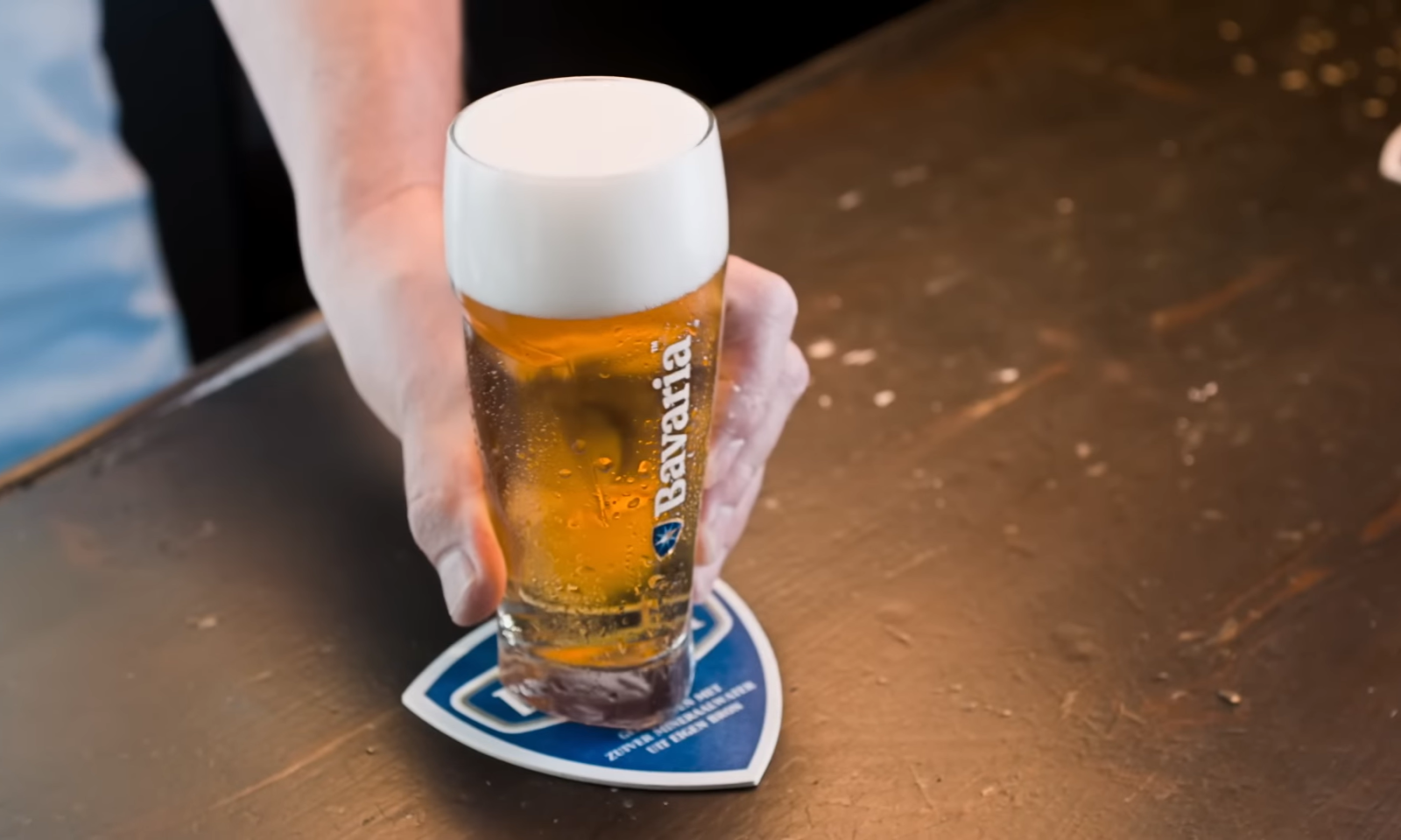 Hand plaatst een glas bier op een bierviltje op een houten tafel.