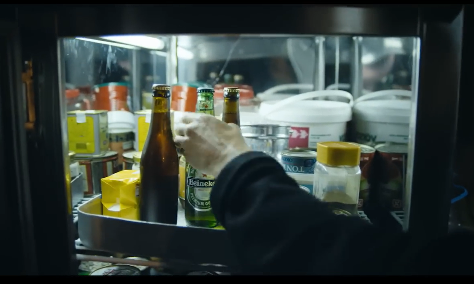 Een hand pakt een Heineken fles uit een koelkast vol voedselproducten.