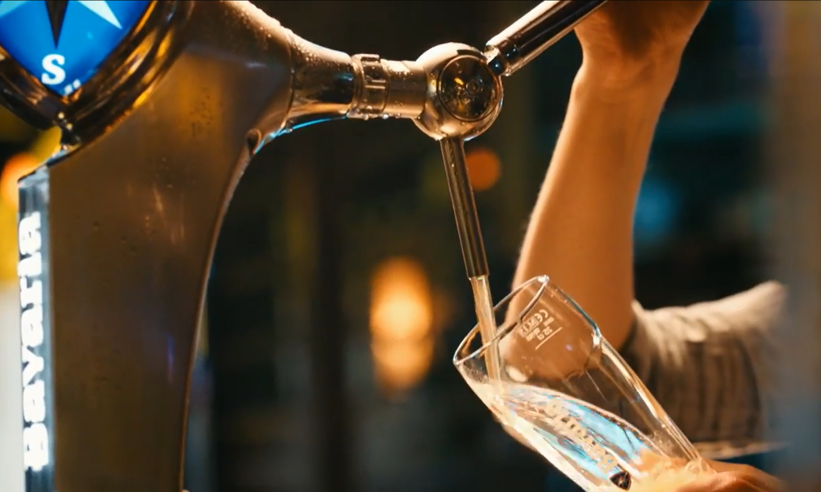 Biertap schenkt helder bier in een schuin glas met merklogo op de achtergrond.