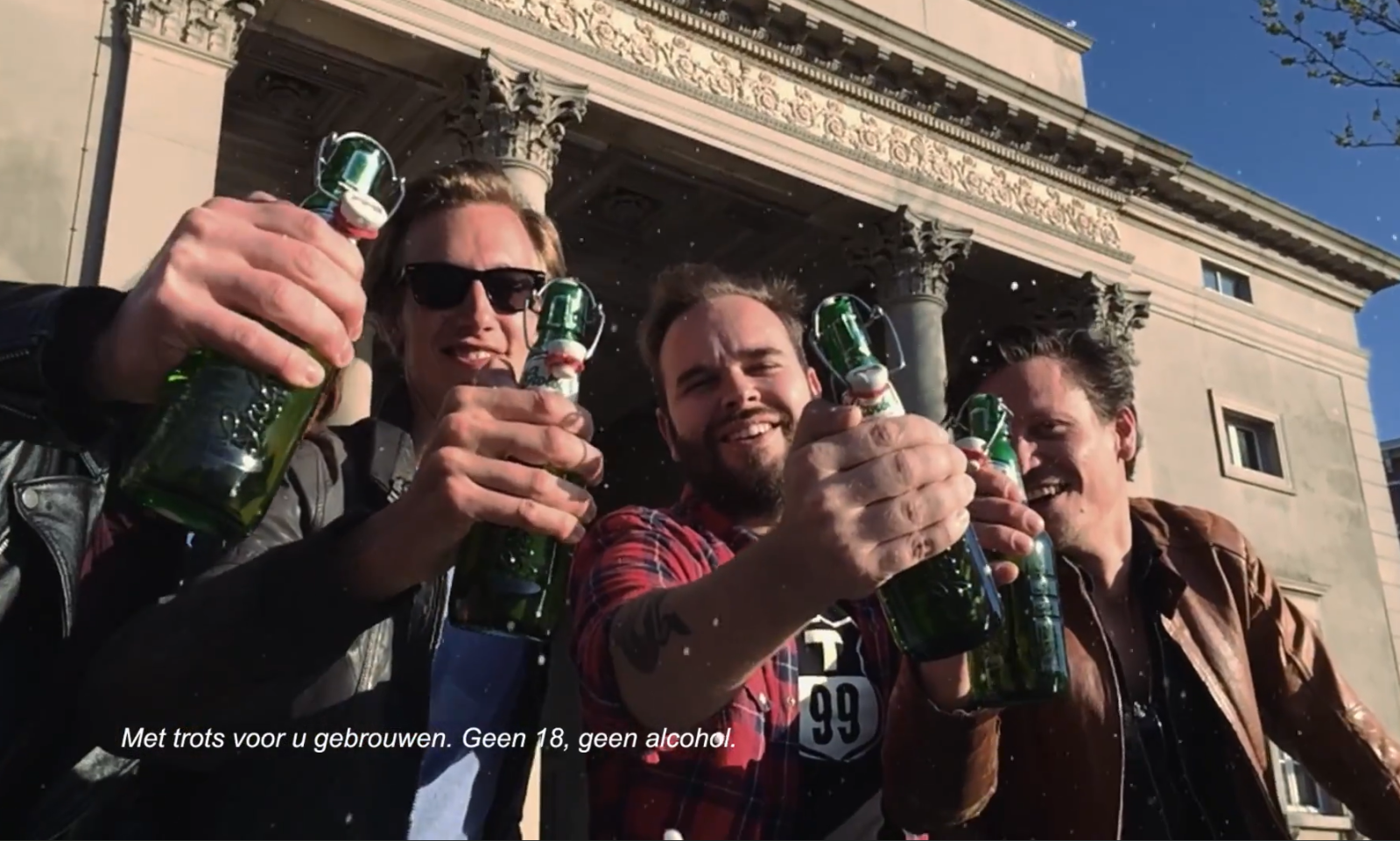 Vier mensen proosten met Grolsch-flessen voor een klassiek gebouw.