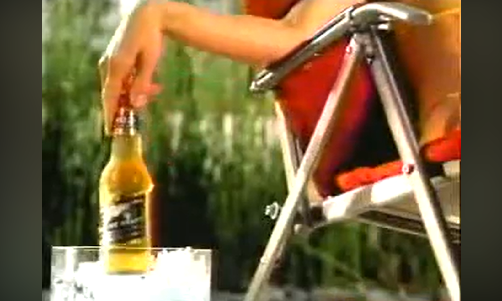 Een hand pakt een fles bier uit een bak ijs naast een klapstoel.