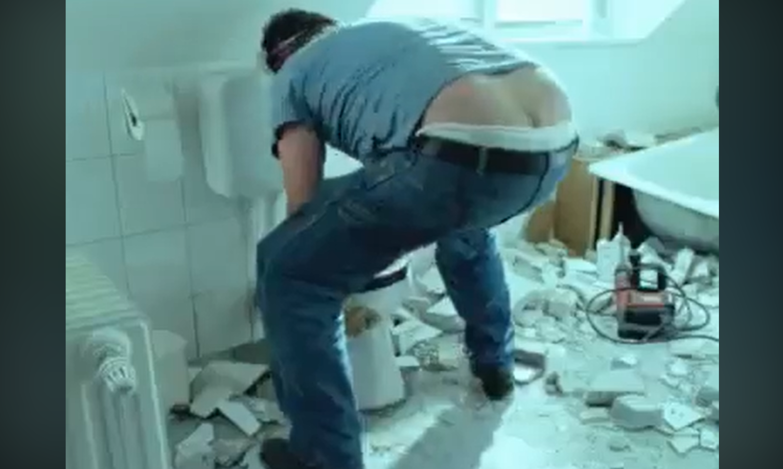 Persoon aan het werk in een rommelige badkamer met tegels op de vloer.