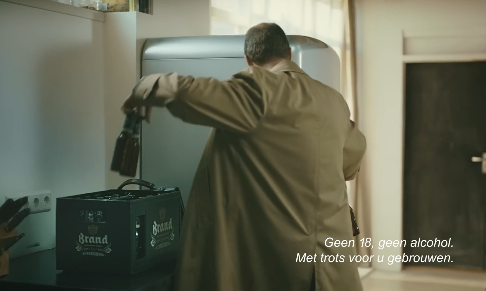 Man in bruine jas plaatst flesjes in een koelkast naast een krat bier.