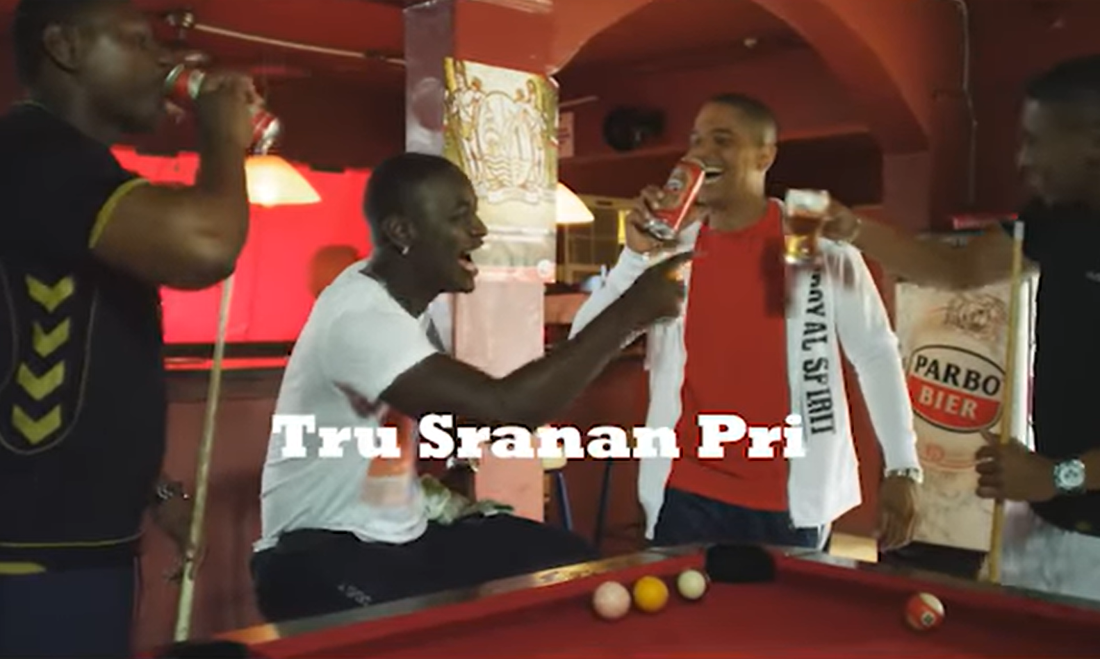 Vier mannen lachen en proosten met Parbo Bier naast een biljarttafel.