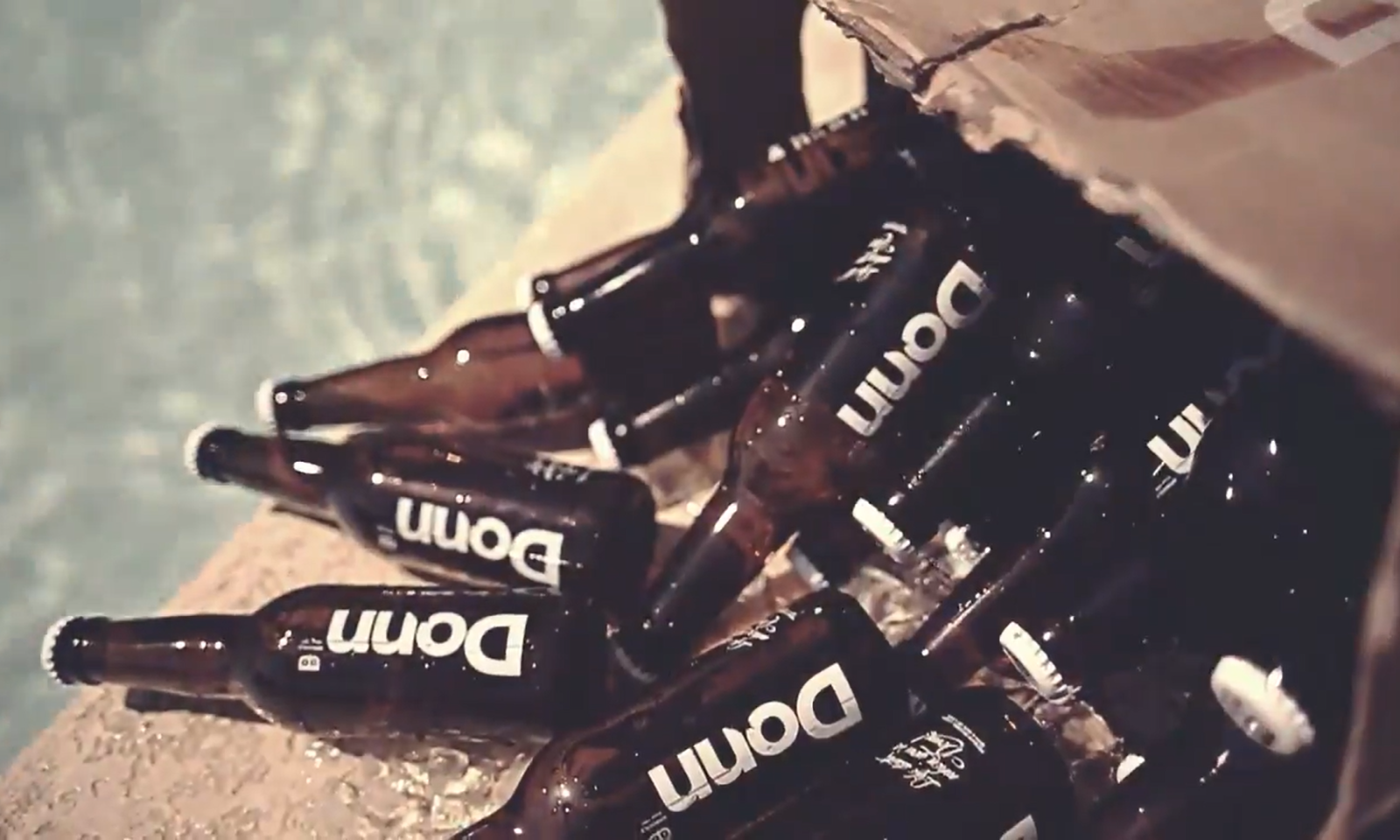 Kartonnen doos met lege Donn bierflesjes, gedeeltelijk zichtbaar op een nat oppervlak.