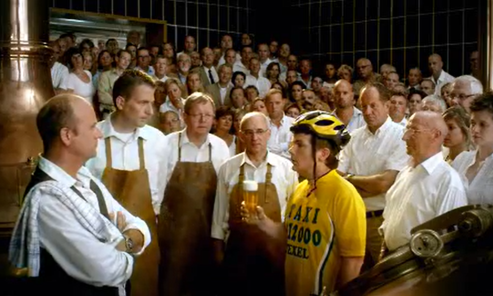 Grote groep mensen in een brouwerij met een fietser die een glas bier vasthoudt.