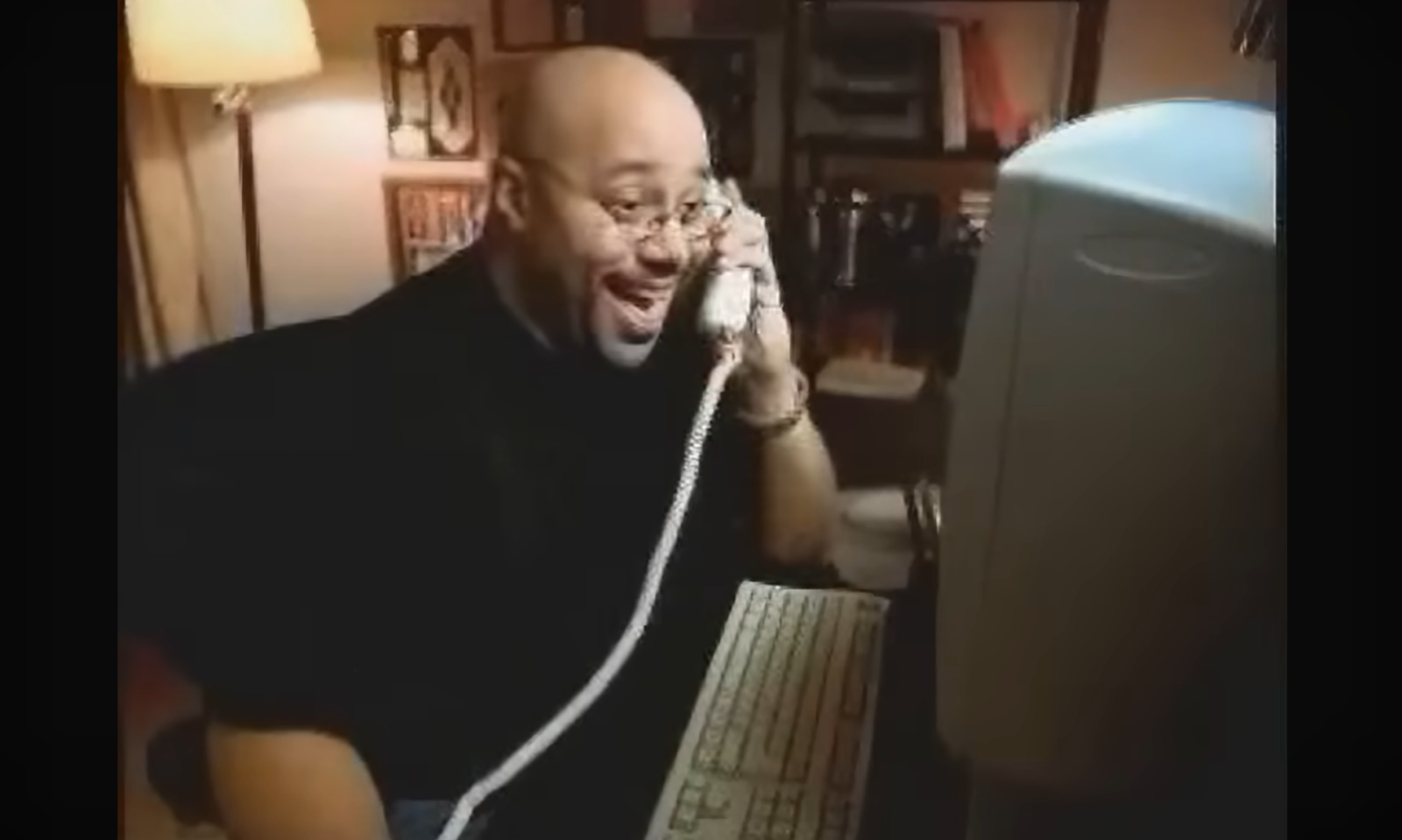 Man lacht terwijl hij aan de telefoon is en naar een computerscherm kijkt.