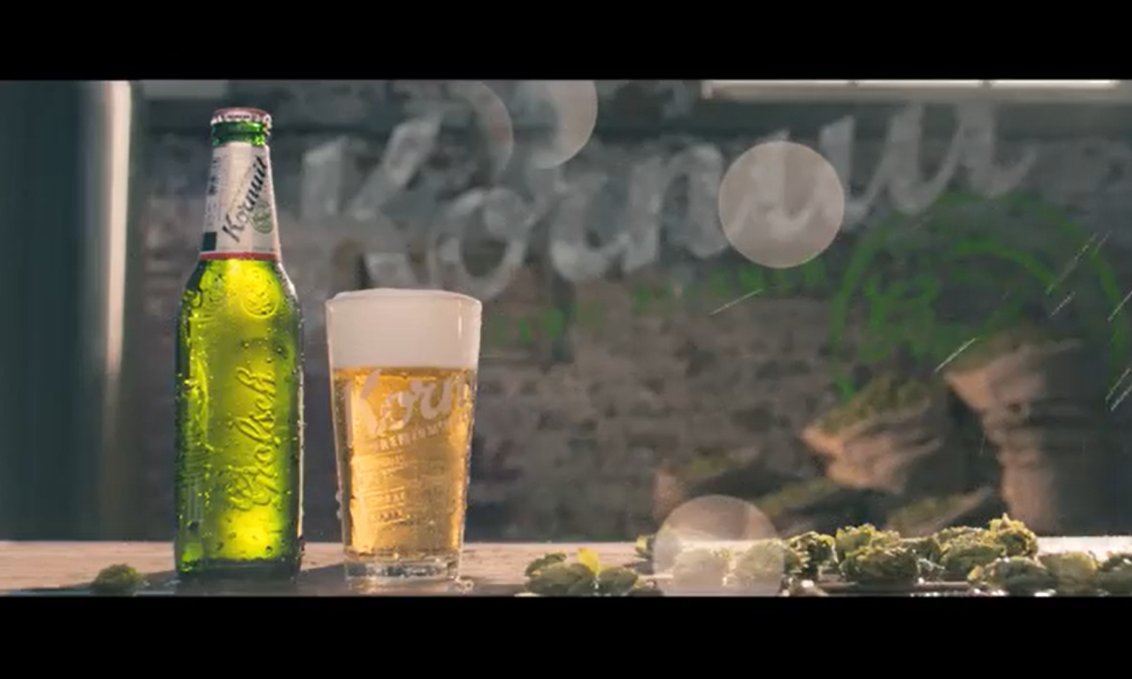 Een fles en glas Grolsch Kornuit bier op een houten tafel met hopbellen.