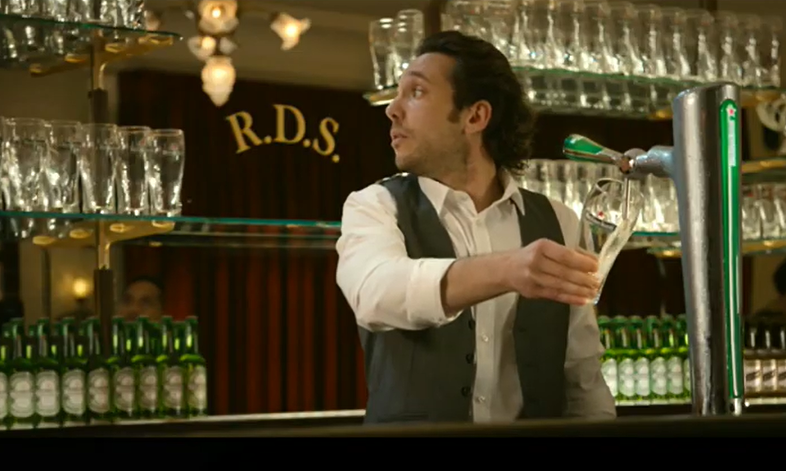 Barman schenkt een glas bier aan een tap in een bar, omgeven door glazen en flessen.