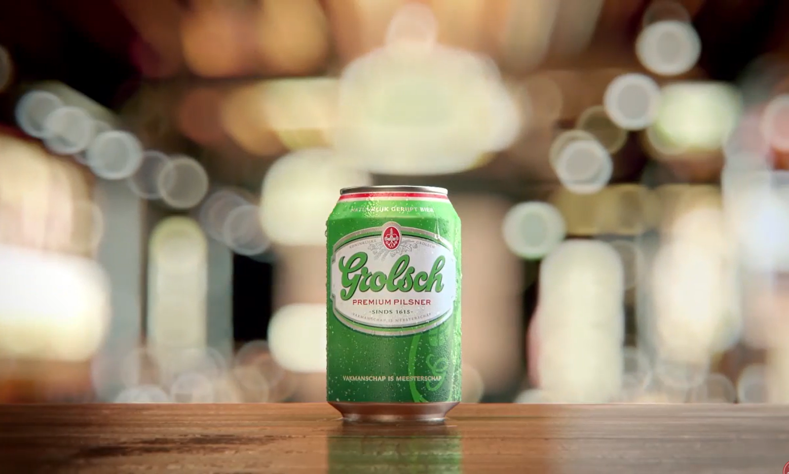 Groene Grolsch bierblik op houten tafel met wazige lichte achtergrond.