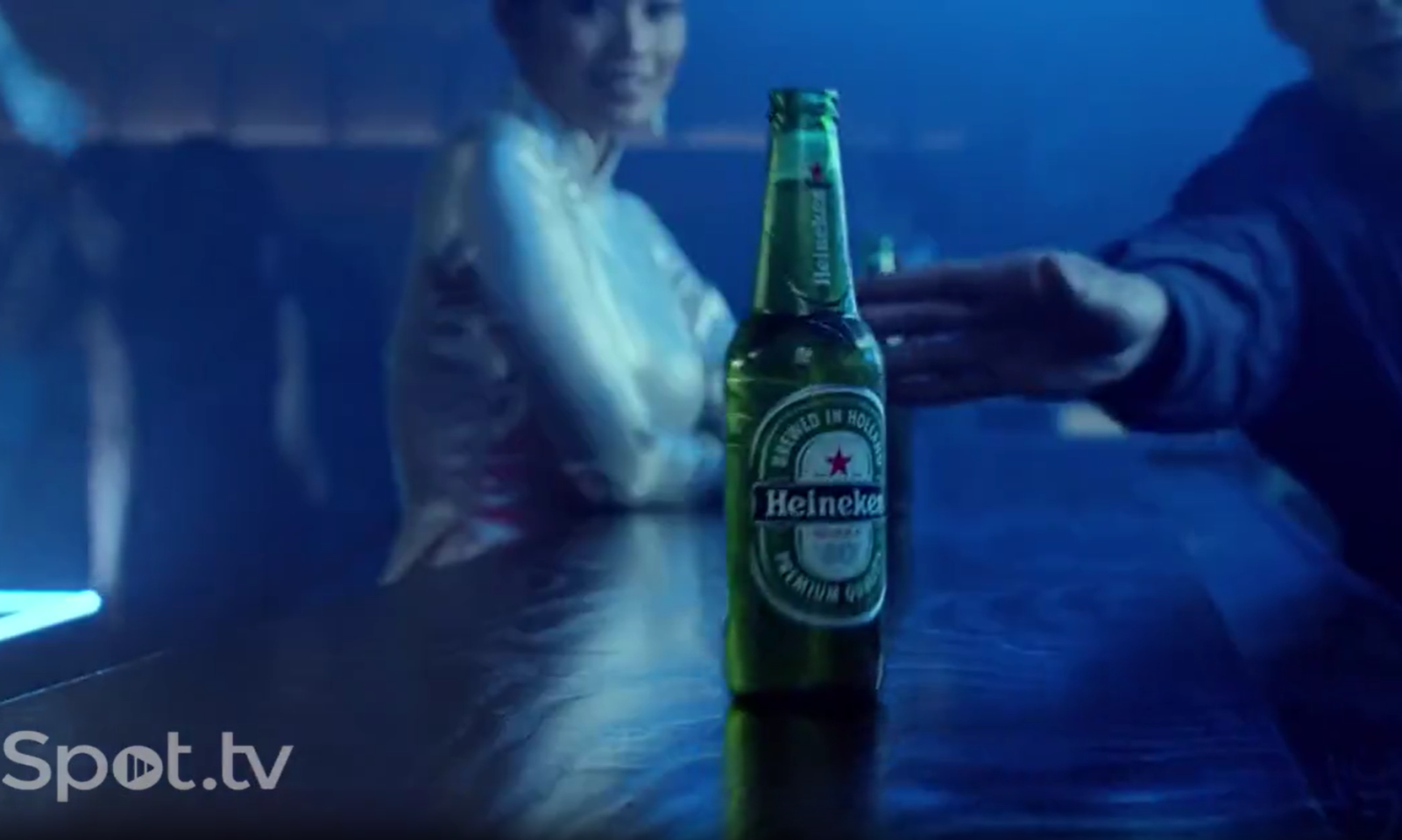 Heineken flesje op een bar met personen op de achtergrond in een clubomgeving.