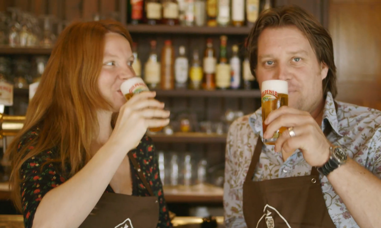 Man en vrouw toosten met een glas bier in een sfeervol café.