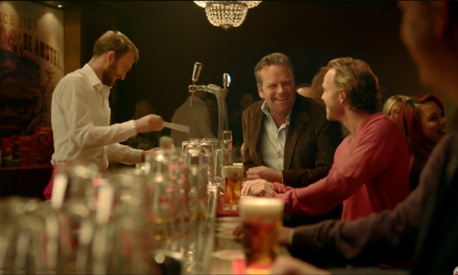 Mensen lachen en praten aan de bar met glazen bier op de voorgrond.