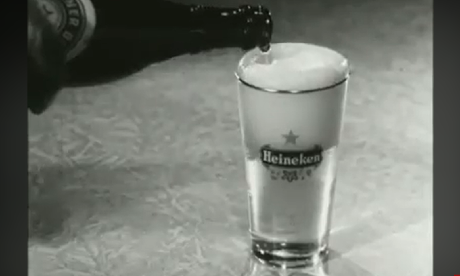 Zwart-wit foto van een Heineken-bierfles die een glas vult.