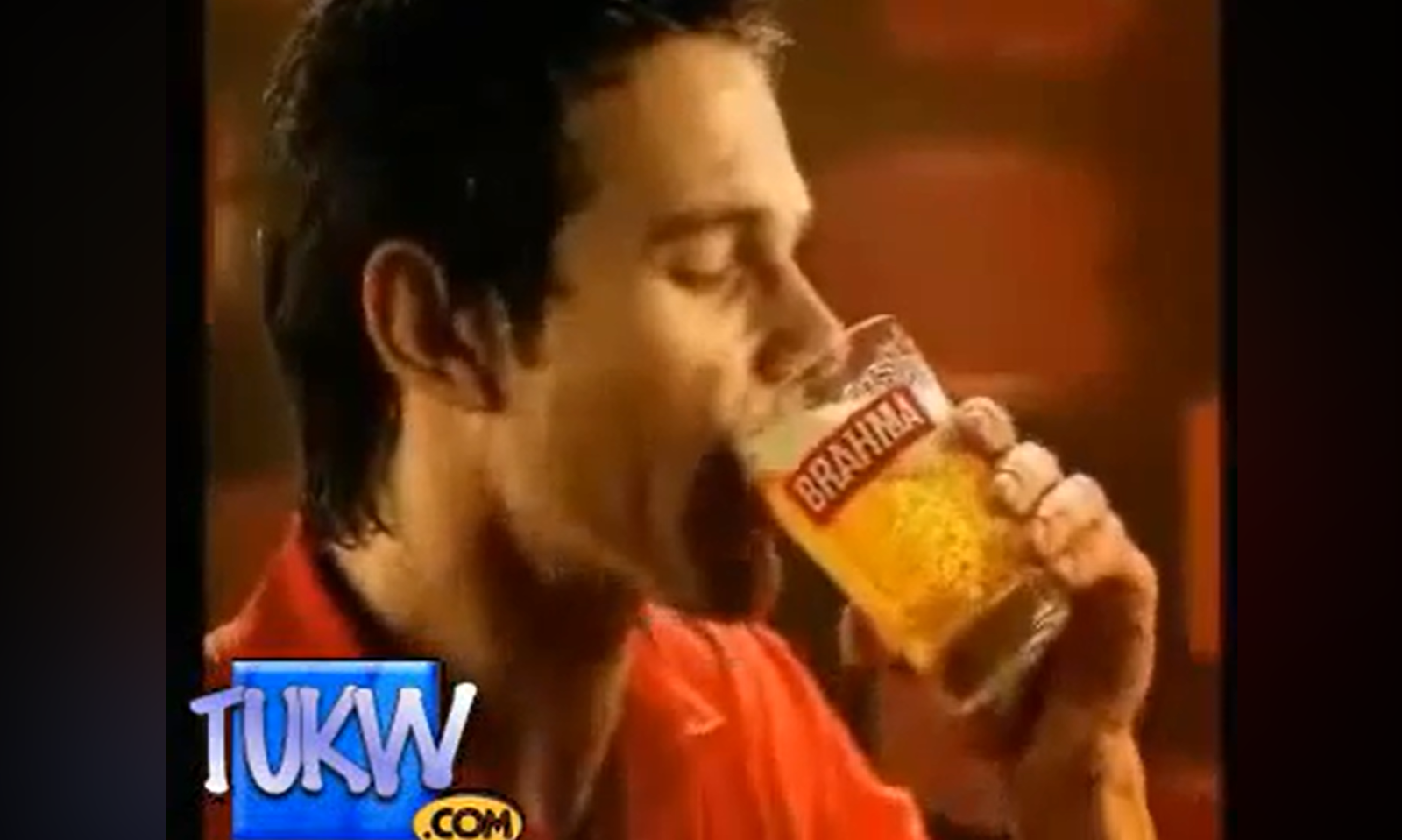 Man drinkt uit een glas bier met het Brahma-logo erop in een warme sfeer.