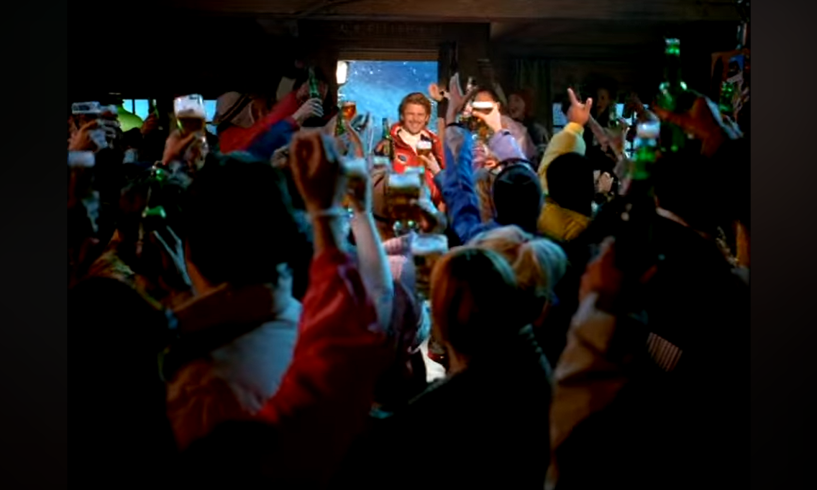 Een groep mensen heft glazen en flesjes bier in de lucht in een feestelijke sfeer.