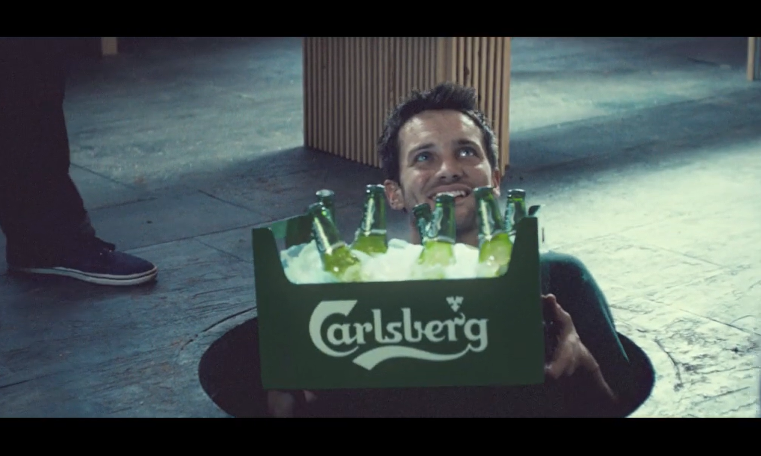 Man met een krat Carlsberg bier komt omhoog uit een gat in de vloer.