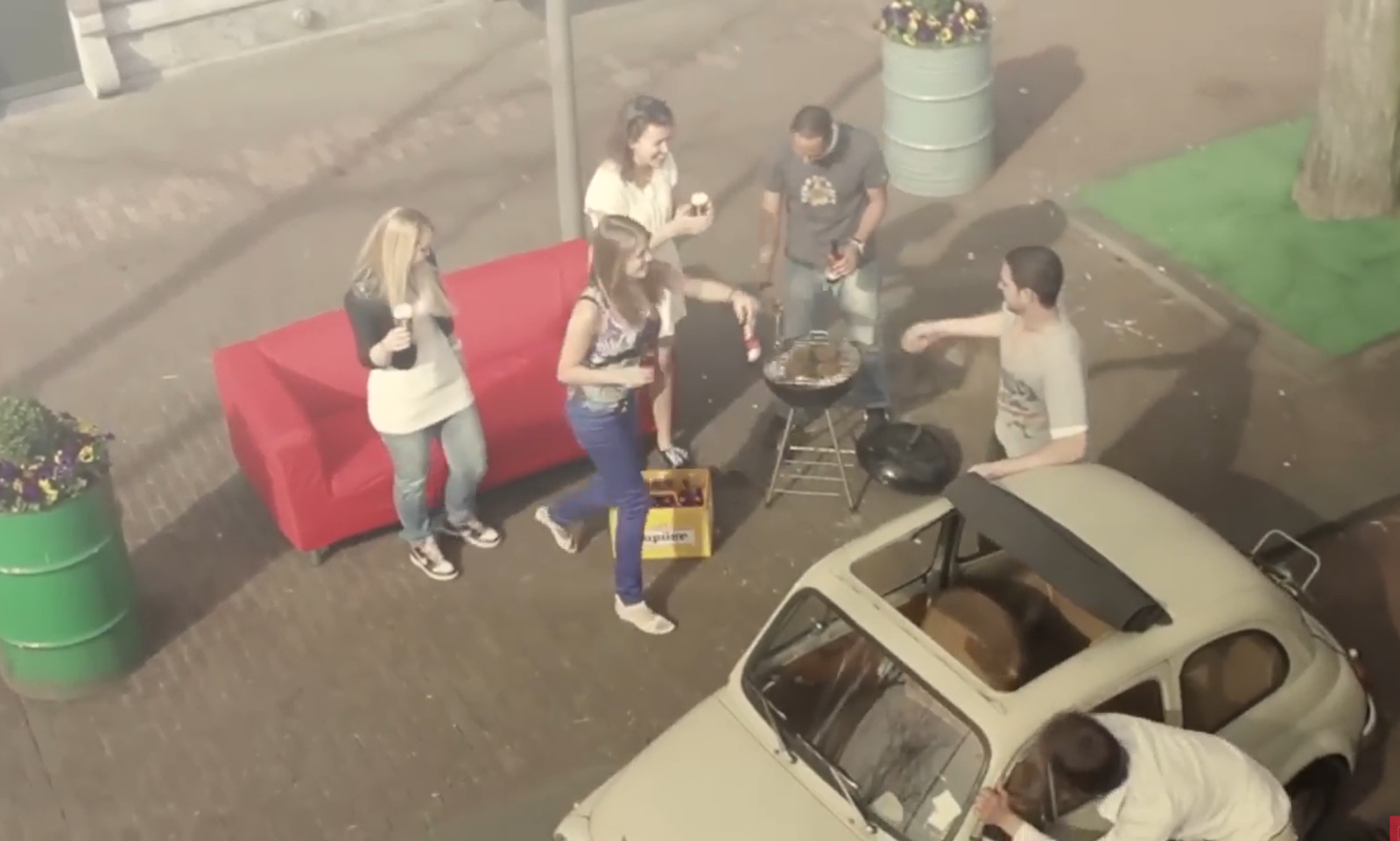Groep mensen barbecuet naast een vintage auto op een parkeerplaats.