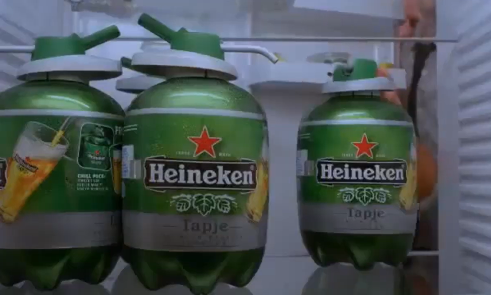 Twee Heineken vaatjes in een koelkast met een persoon op de achtergrond.
