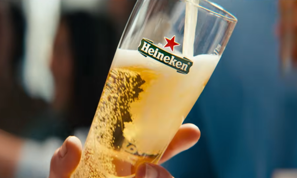 Hand houdt een halfvol glas Heineken bier vast terwijl het wordt gevuld.