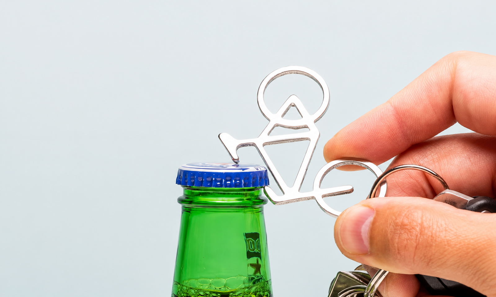 Hand gebruikt een metalen fiets-flesopener aan een sleutelbos op een groene fles met blauwe dop.