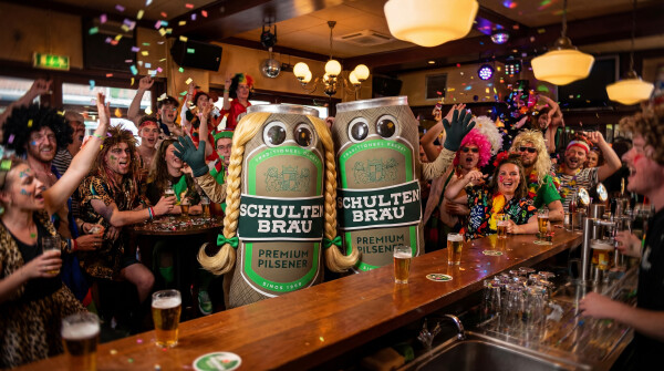 Mensen in een bar gekleed in carnavalskostuums met grote bierblik kostuums die op de voorgrond staan.